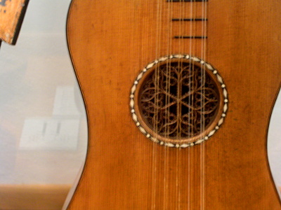 [A view of the hole in the body of the guitar. There is a white color detail (possibly pearl inlay) around the hole. The hole itself has a lace effect wood carving within it.]